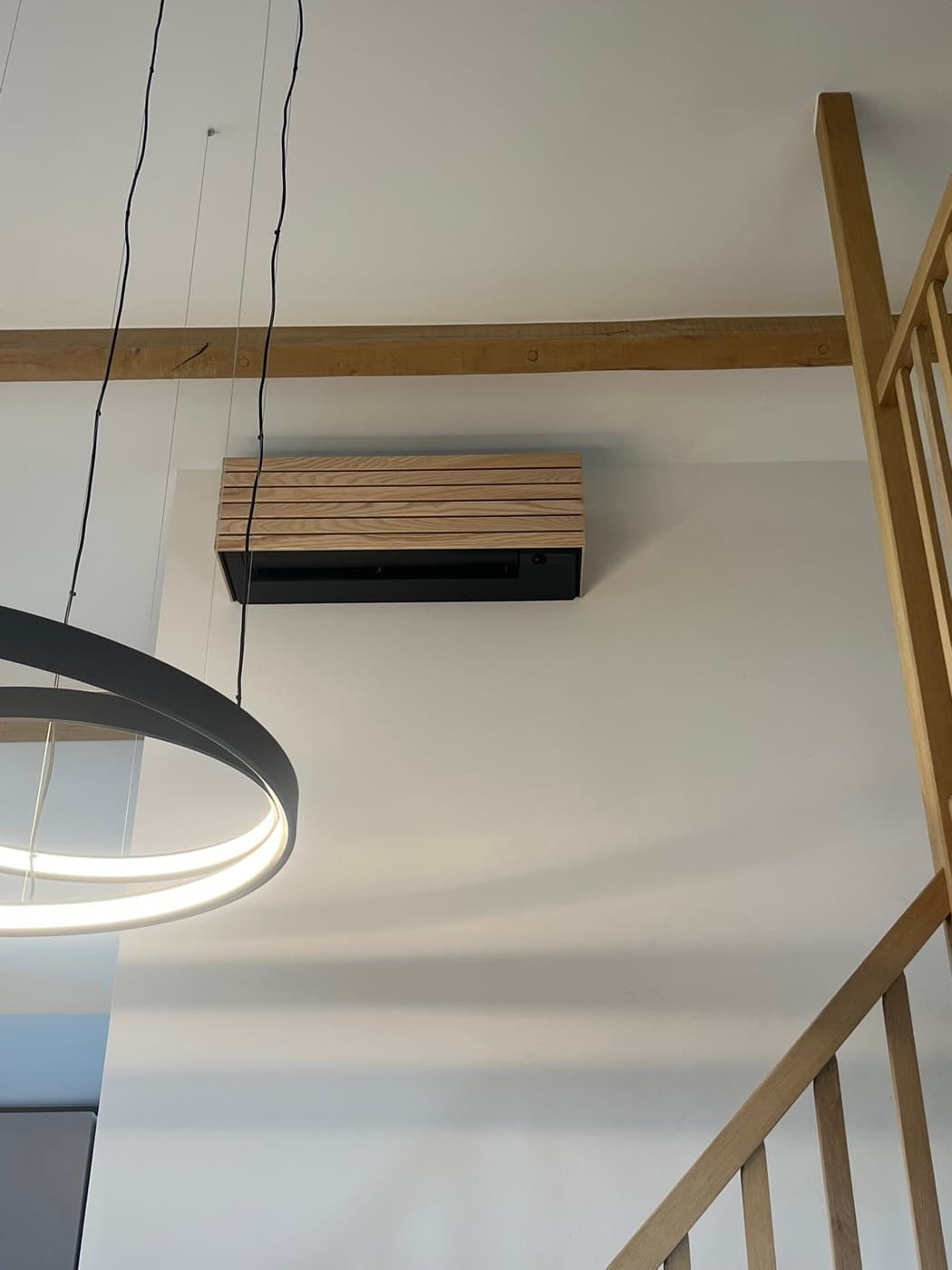 Airco-binnendeel weggewerkt achter een eikenhouten lamellen-omkasting in een woonruimte met vide