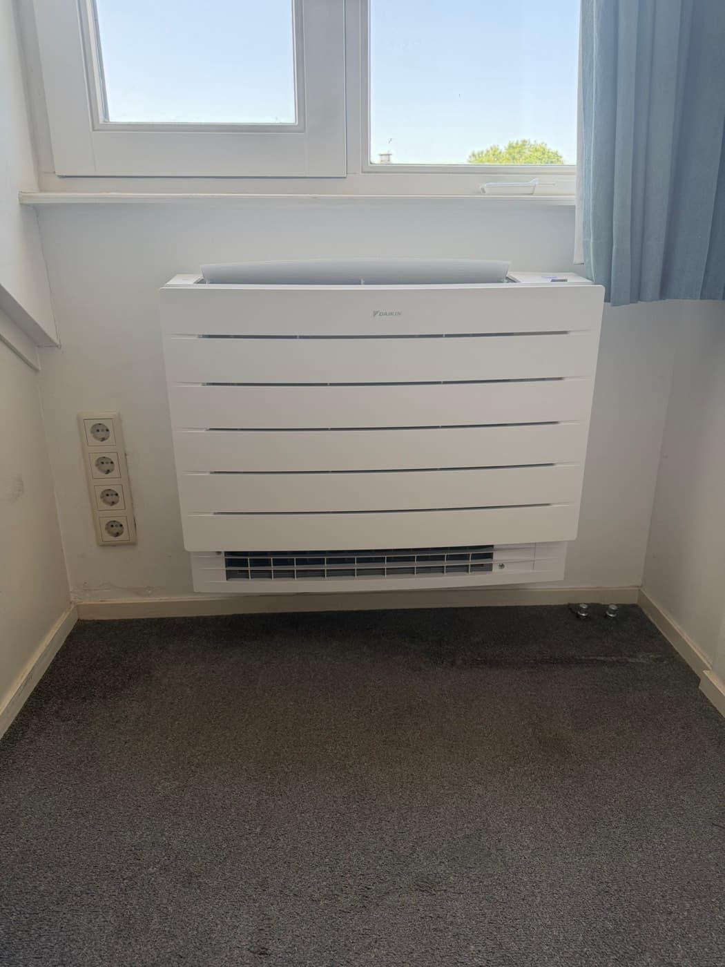 Daikin Perfera-vloermodel airco onder een raam in een slaapkamer