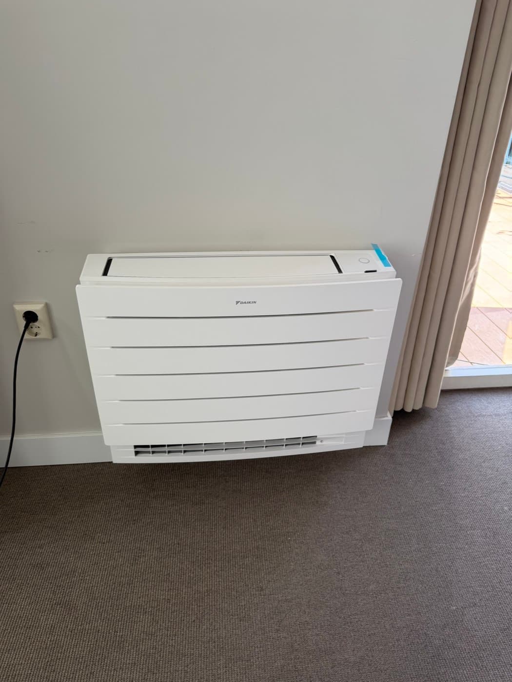 Daikin-vloermodel airco naast openslaande tuindeuren in een woonkamer